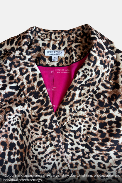 Close-up of a leopard print top by Peak Women, featuring a beige, brown, and black animal pattern with a vibrant hot pink inner lining visible at the collar.
