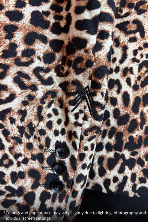 Close-up of a leopard print fabric garment, likely a blazer or jacket, showing the pattern, black buttons, and a small black embroidered detail on a beige background.