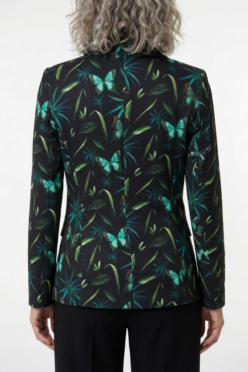 A person shown from the back wearing a tailored blazer with a black base and an allover tropical print of green leaves and turquoise butterflies, paired with black trousers against a plain light background.