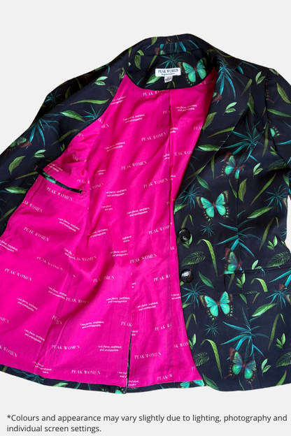 A men's blazer laid flat on a speckled stone floor, featuring a vibrant hot pink patterned lining and a dark navy outer fabric printed with green tropical leaves and turquoise butterflies. The brand name 'PEAK BOYA' is visible on the inner lining.