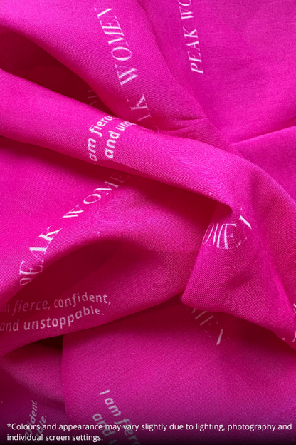 Bright pink sheer fabric with white printed text reading 'PEAK WOMEN' and 'fierce, confident, and unstoppable.' draped in soft folds.
