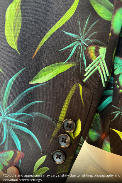 Close-up of a dark tropical print fabric with green leaves, turquoise palm fronds, and butterfly motifs, featuring three dark buttons on the sleeve.